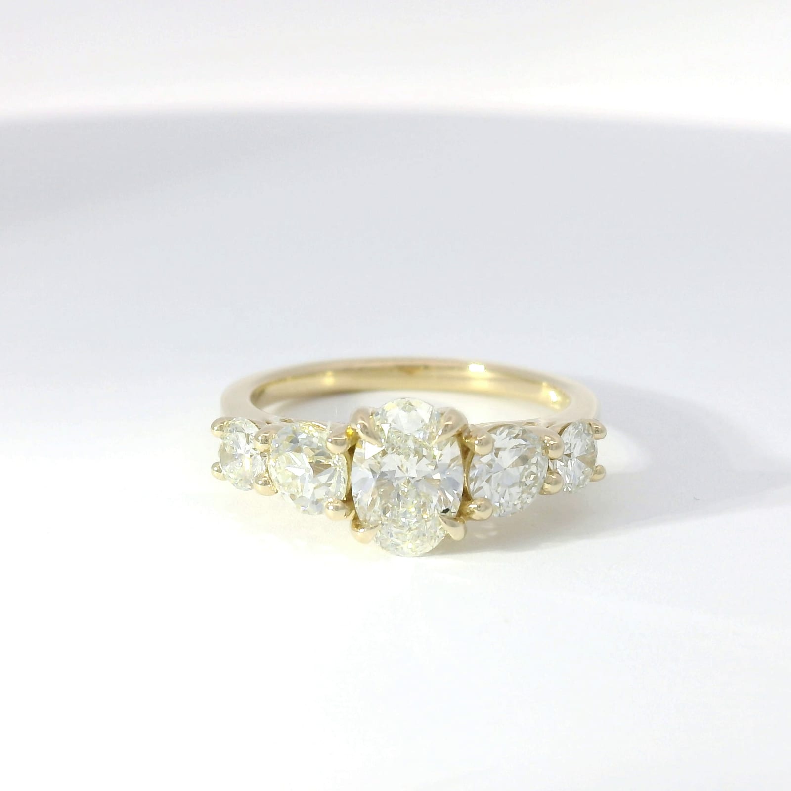 Oval diamond center flanked by graduated round diamond five-stone setting in yellow gold