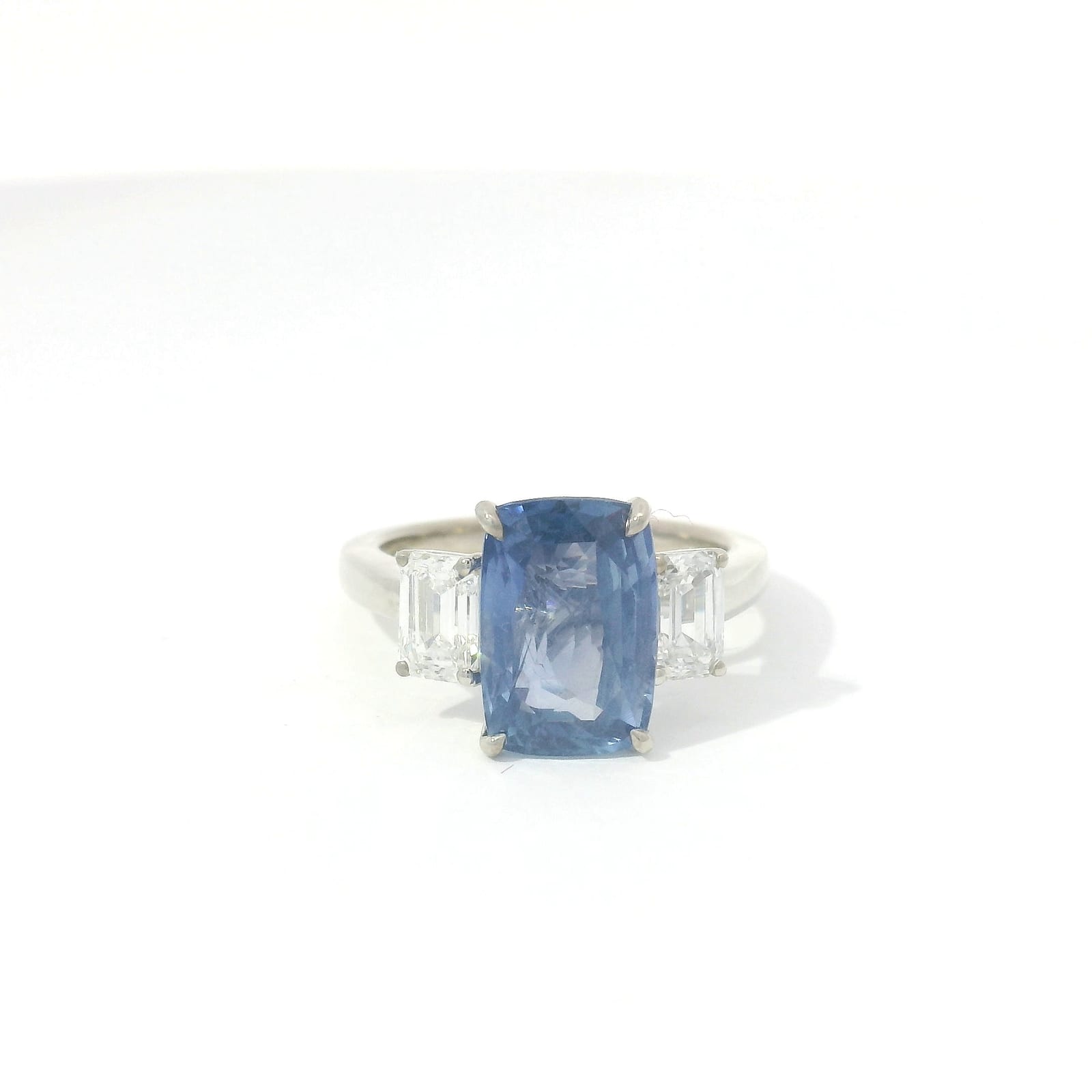 Cushion-cut blue sapphire three-stone engagement ring in platinum with trapezoid diamond sides