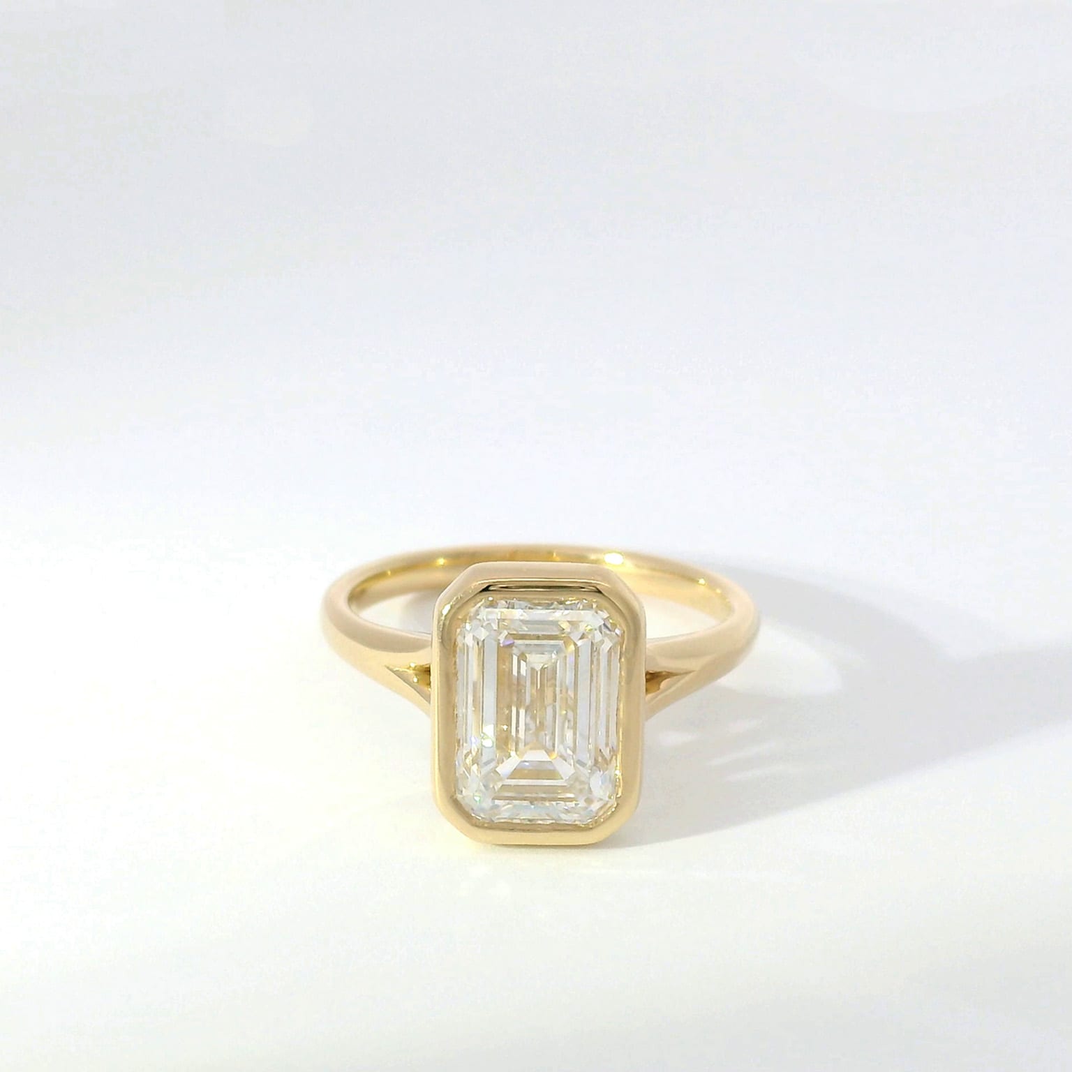 Emerald-cut diamond bezel-set solitaire in yellow gold with split-shoulder band